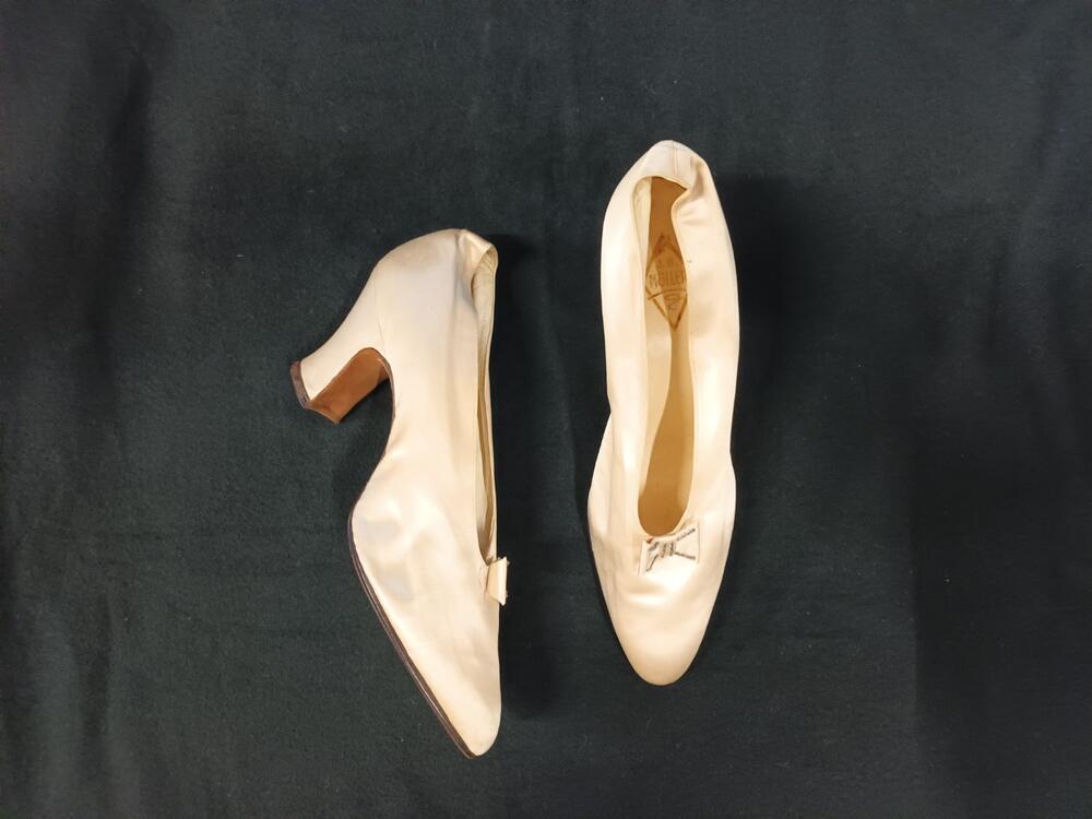 1 paar trouwschoenen, pumpmodel, voet en hak bekleed met ivoorwit satijn. Garnering van strikje van…