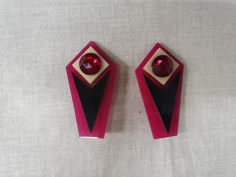 1 paar oorclips van roze kunststof. Pijlvormig model met geometrische figuren in zwart en wit. Rode…