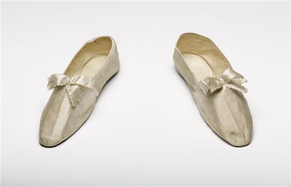 Schoentjes van wit satijn, op de voorschoen een strik van wit satijnlint. Geheel platte schoenen…