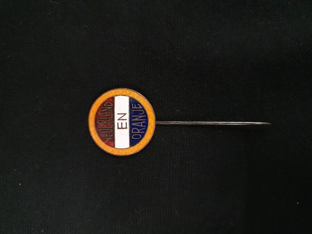 Speld, rond geëmailleerd plaatje met achtergrond in de kleuren van de Nederlandse vlag en oranje…