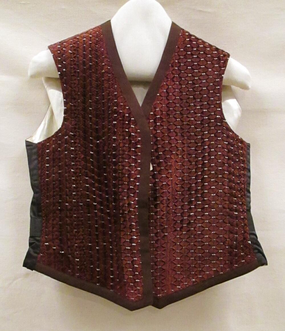 Vest (man) van bruinrood ribfluweel in schubvorm gewoven en afgezet met een bruin wollen band,…