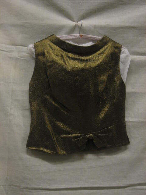 Hesje van goudkleurig lurex, , mouwloos getailleerd model met 2 strikken van idem stof, onderdeel…