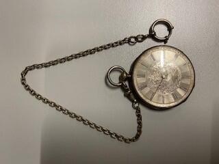 Horloge aan ketting, rond model van zilver, enerzijds klokje tegen voorstelling van putti en…