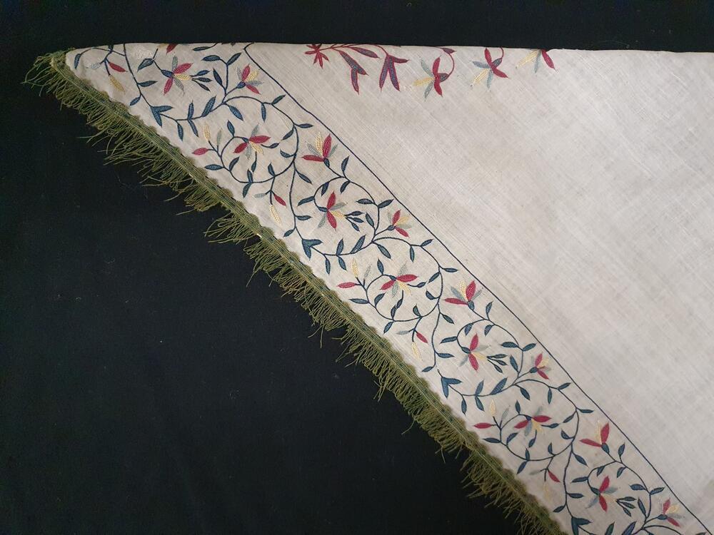 Fichu van neteldoek met rand in tamboureerwerk: kleurige bloemen, groene franje. Op japon O.W. 27