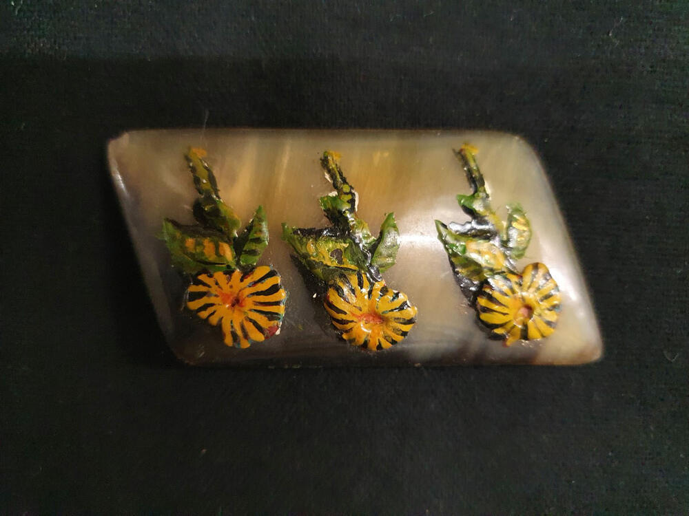 Verzetsbroche. Ruitvormige broche, bruin/beige, met applicatie van 3 gele margrieten met groene…