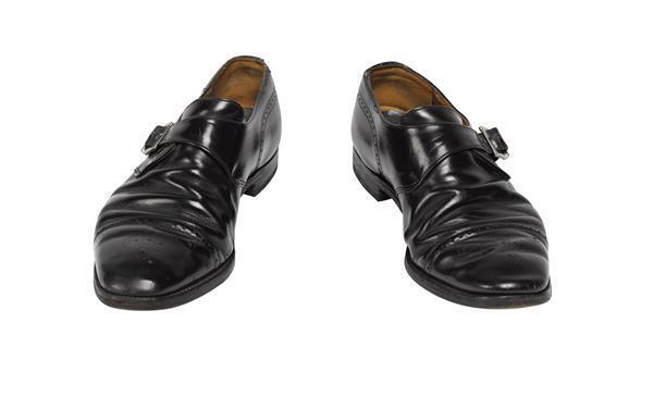 Een paar mannenschoenen, model van zwart leer met gesp, en patroon van kleine gaatjes bij neus