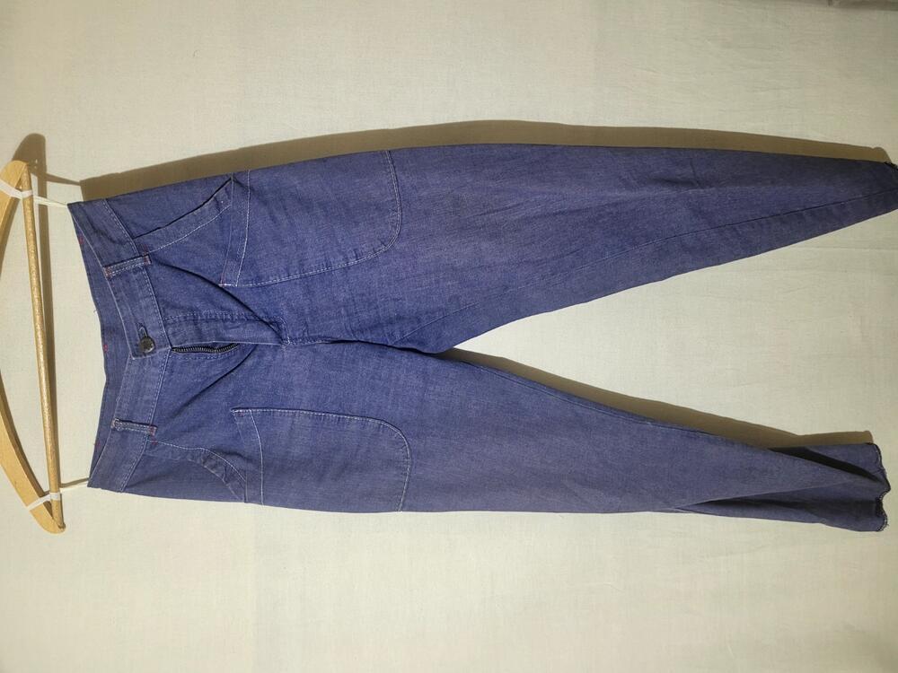 Lange broek van blauw denim met witte en rode stiksels. Model met toelopende pijpen en opgestikte…