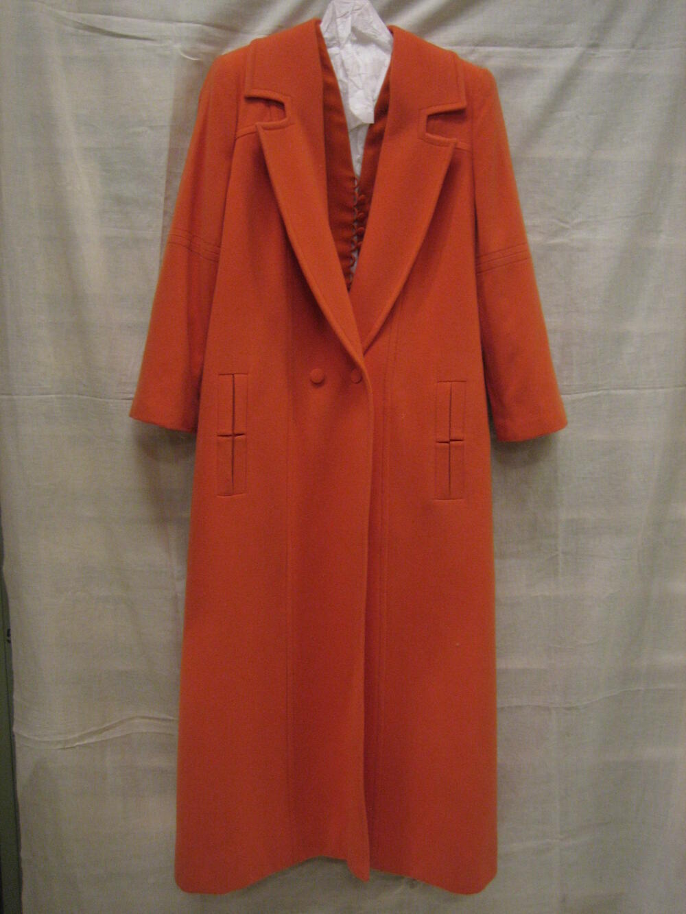 Ensemble van oranje wol en oranje satijn, bestaande uit broekpak, (maxi)jas, halsband en hoed met…