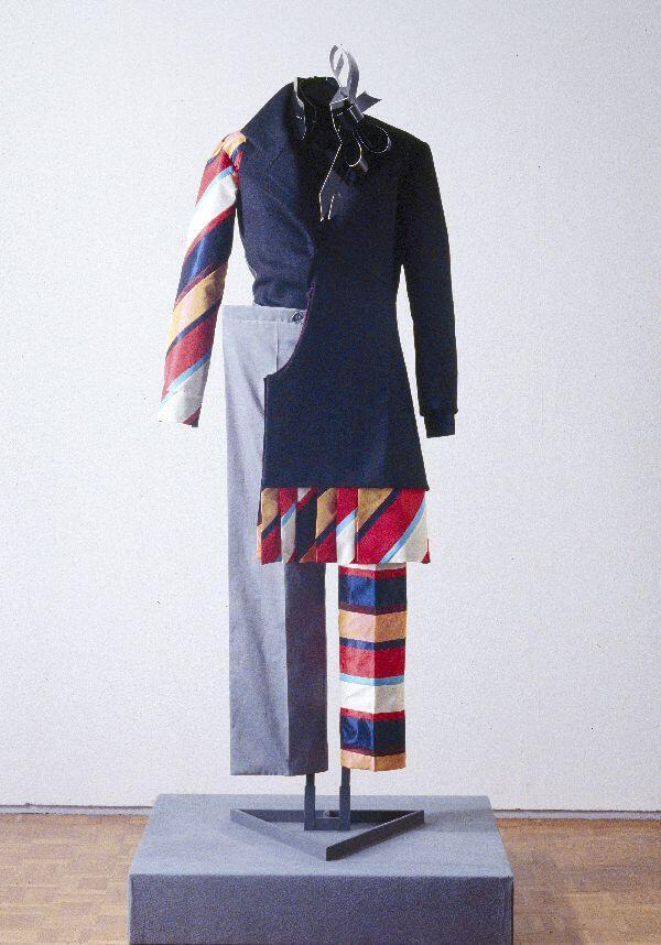Pak, jas en broek van zwarte wol en meerkleurige synthetische stof in asymmetrische vorm. Jas met…