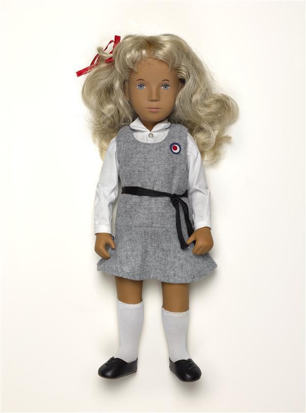 Meisjespop 'Sasha', gekleed in witte blouse, grijze overgooier met zwart ceintuur, witte…
