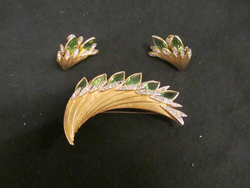 Broche en oorclips, veervorm van goudkleurig metaal met witte pastestenen en groene imitatieperidots