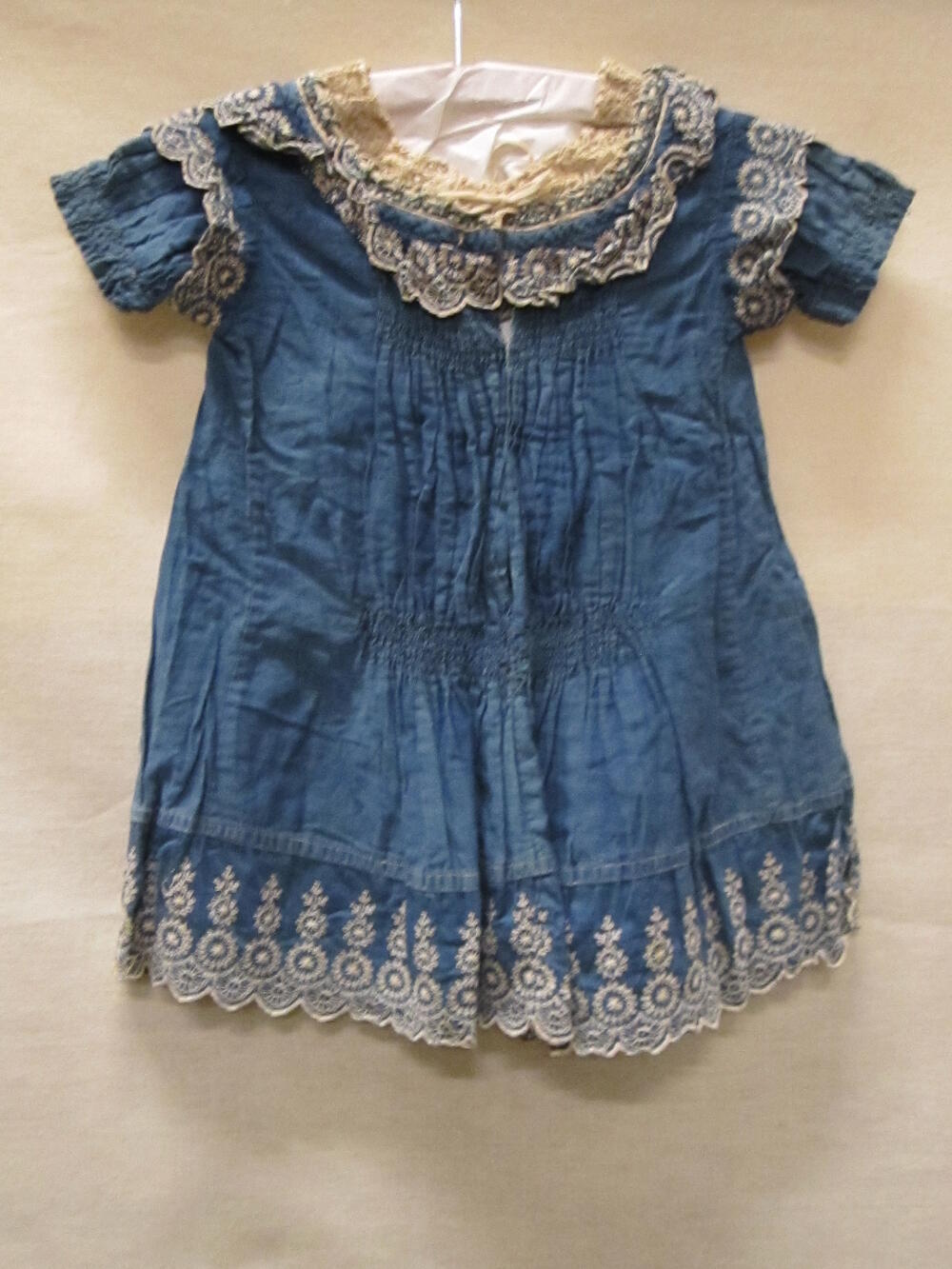 Jurk (kind) van blauw katoen met witborduursel om hals, pofmouwen en zoom. Om hals haakwerk van…