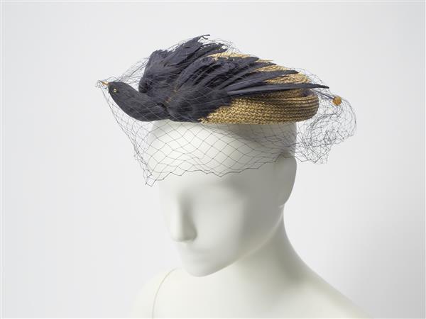Hoed van beige stro, gegarneerd met donkerblauwe/zwarte vogel