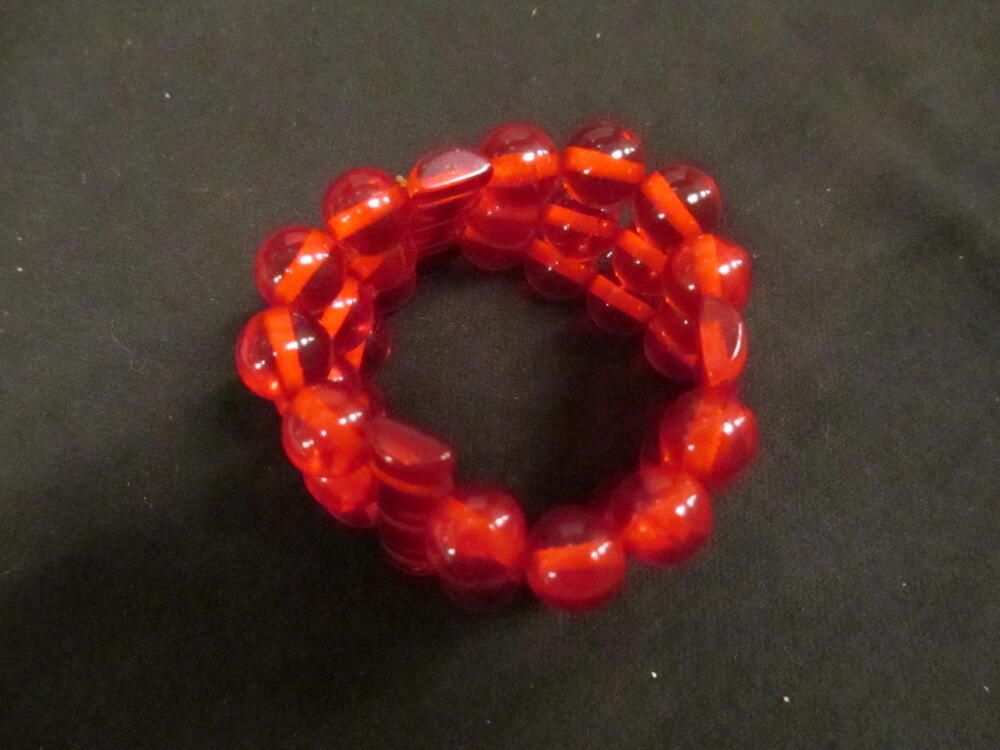Armband, drie strengen semitransparante rode plastic kralen waartussen langwerpige kralen van idem…