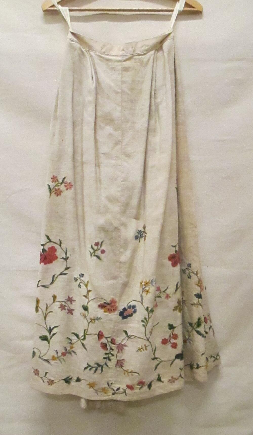 Rok van wit linnen, ondergedeelte met wollen crewelwork van bloemranken in diverse tinten groen,…