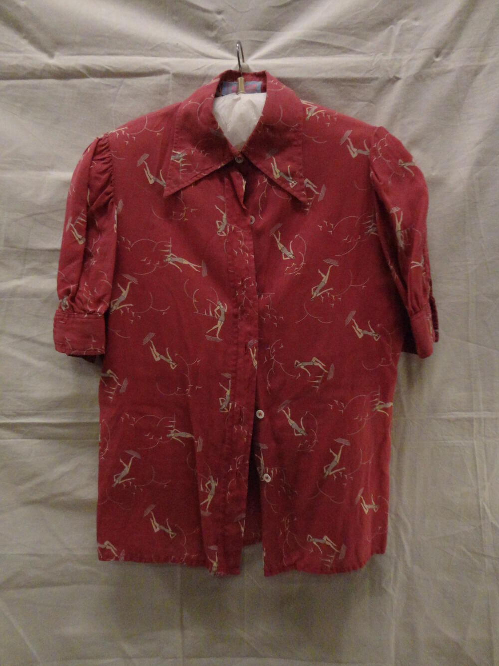 Blouse van (oud)rode katoen met korte kopmouw en manchet met dessin van zwemster in grijs badpak,…