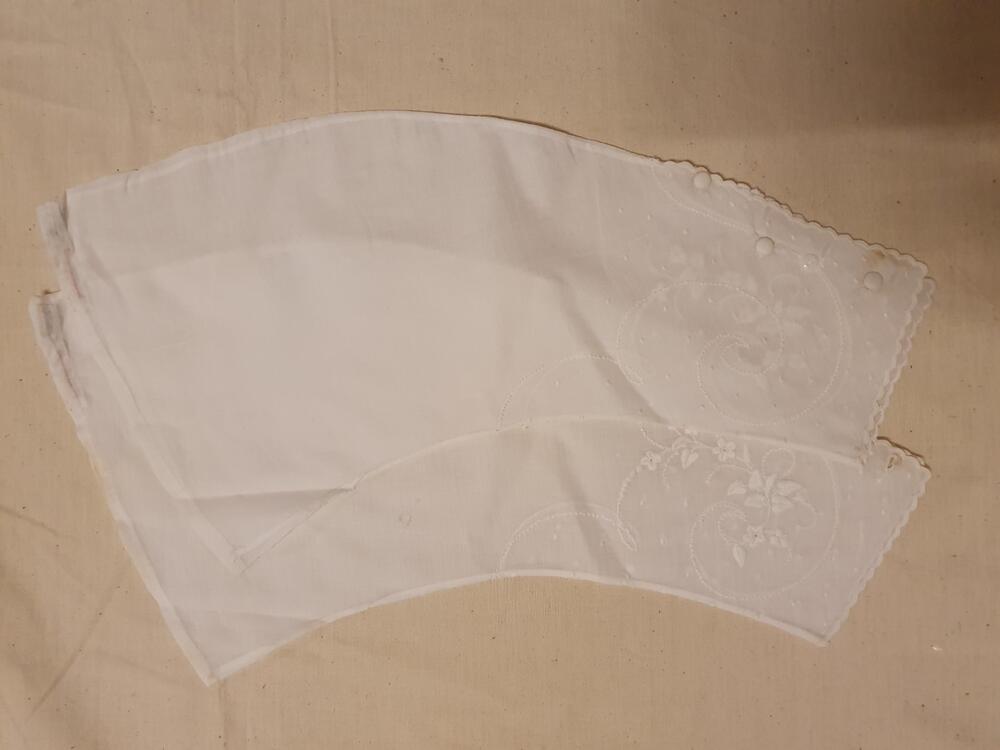 Jasje (baby) van beige zijde, langs de hals afgebiesd met rood zijden lint, voering van grof wit…