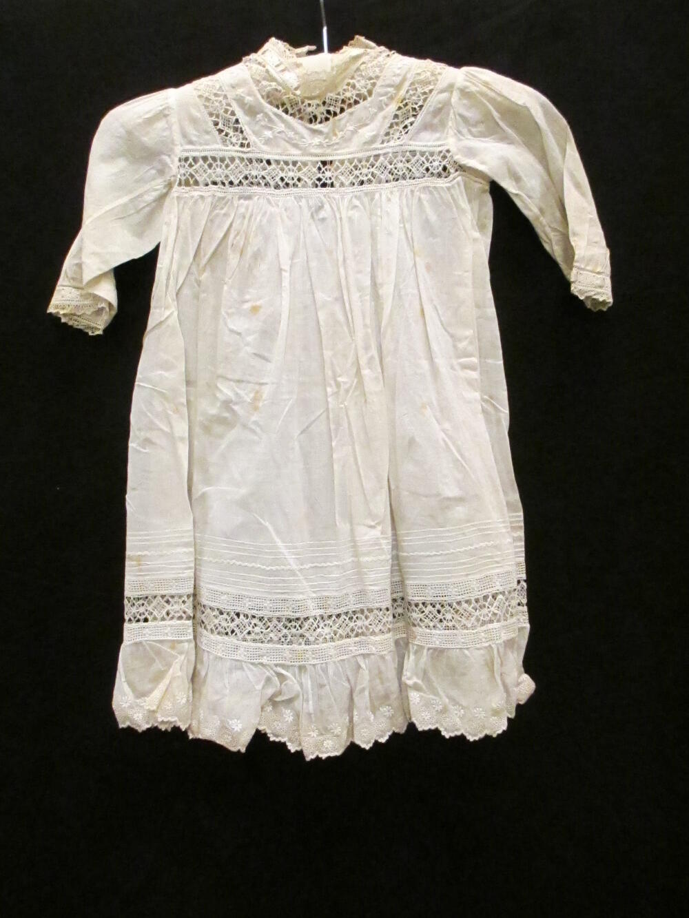 Jurk (kind) van wit katoen (batist?), gegarneerd met kloskant en broderie