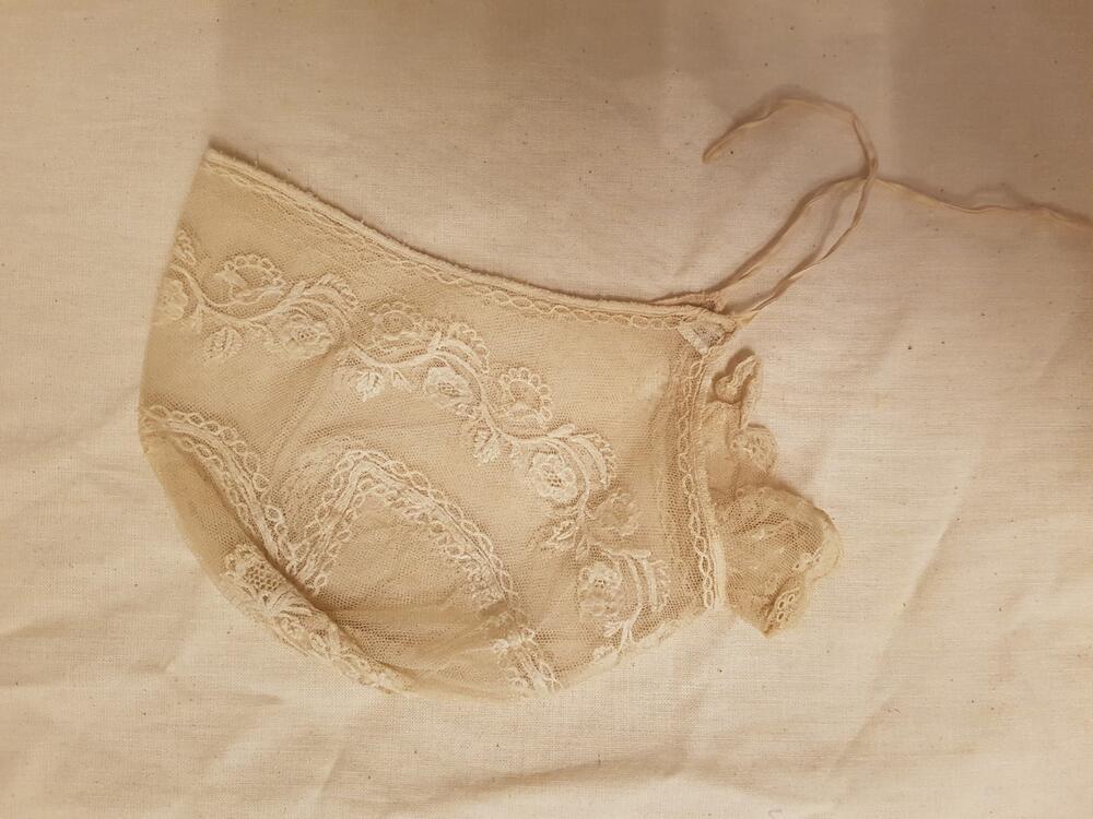 Damesmuts, bestaat uit een om het hoofd sluitende pas van witte tule, versierd met een bloemslinger…