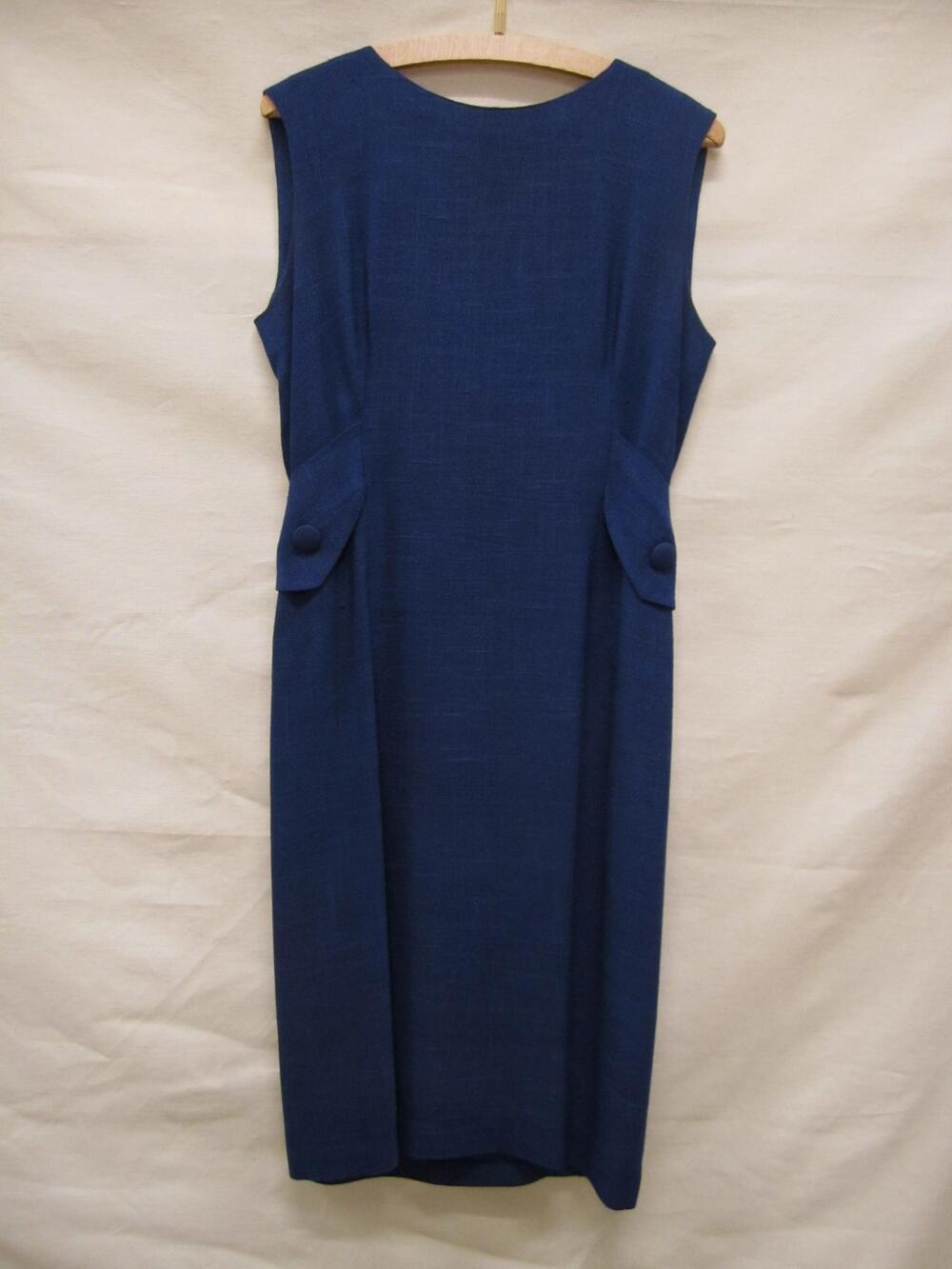 Jurk van blauw linnen, halflang, mouwloos model met op taillehoogte naar achter toe lopend half…