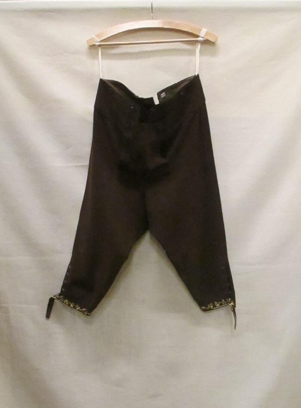 Broek (man) van bruin laken met geborduurde randen van kleurige bloemen, behorende tot pak