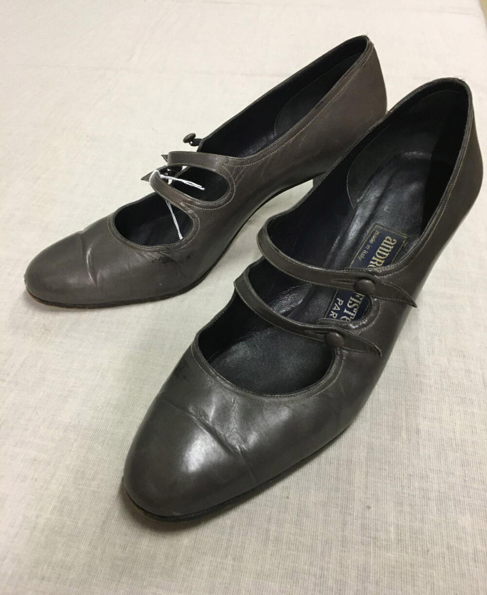 Dames schoenen. Pump model met 2 wreef bandjes met knoop sluiting. Grijs leer, hoge bruine hak.