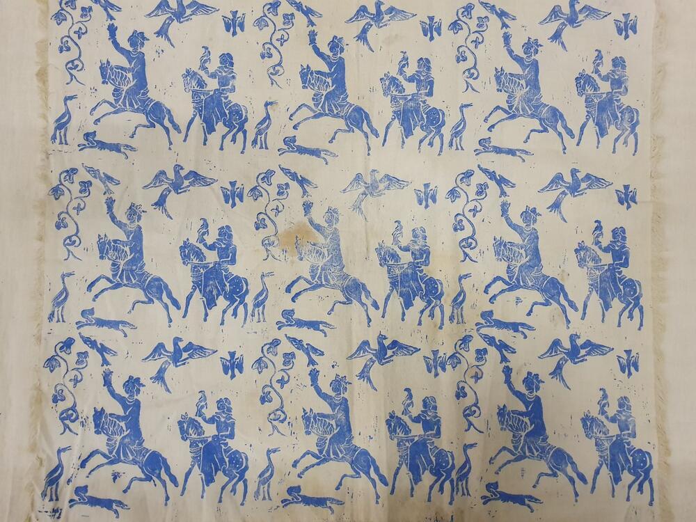 Rechthoekige lap van katoen bedrukt met vrouwenfiguren in blauw, bezig met valkenjacht