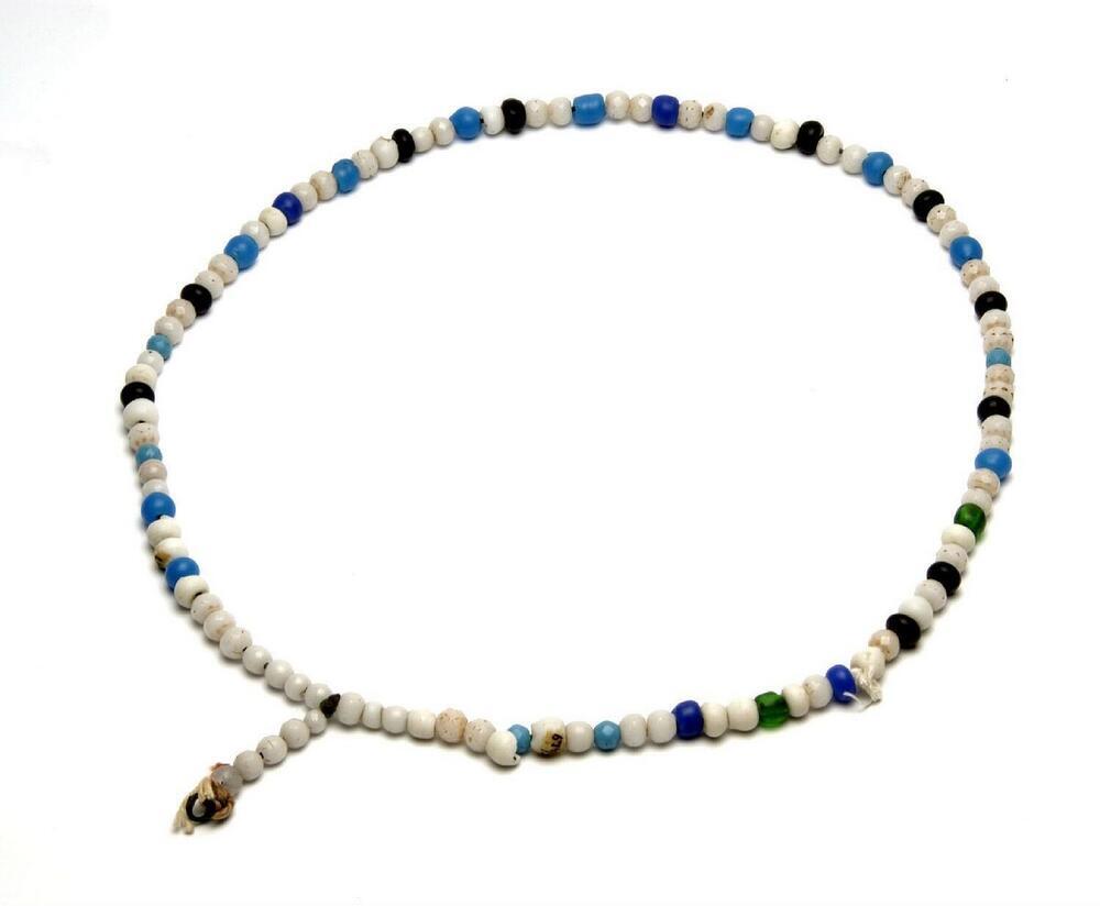 Halsketting van witte glaskralen, afgewisseld met blauwe, groene en zwarte kralen, gedragen door…