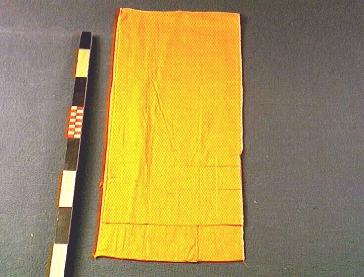 Een oranje mousseline vest, onderdeel van een vijfdelige kledingset van een noviet.
