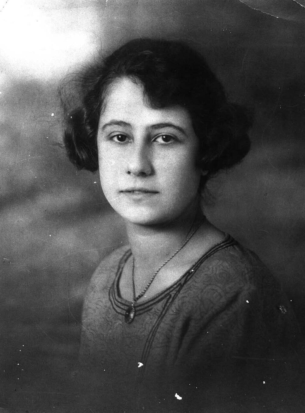 Portret van een jonge vrouw met half lang, donker, krullend haar een een ketting om haar hals