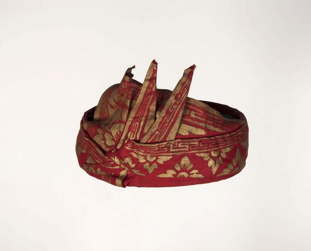 Opgemaakte hoofddoek, gevouwen van rode katoen met ornament in bladgoud