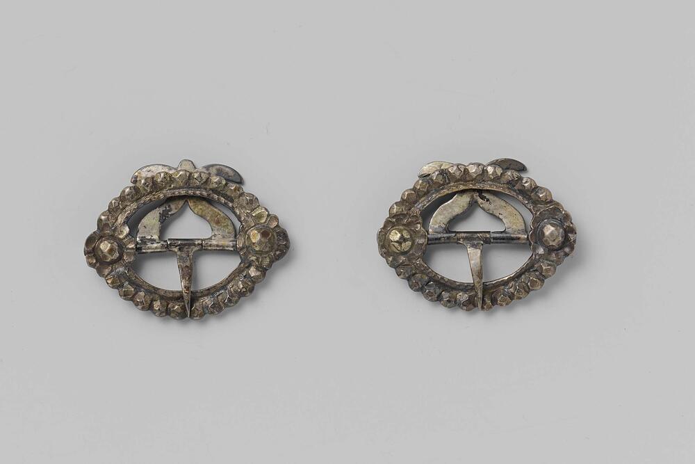 Gesp van zilver, ovaalvormig met twee bloemen in reliëf in de hoeken van de vatting