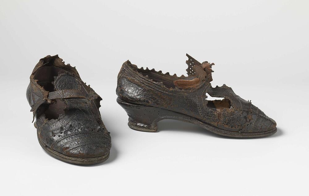 Schoen van zwart runderleer met lage sleehak, ronde neus en een voorblad eindigend in een klep…