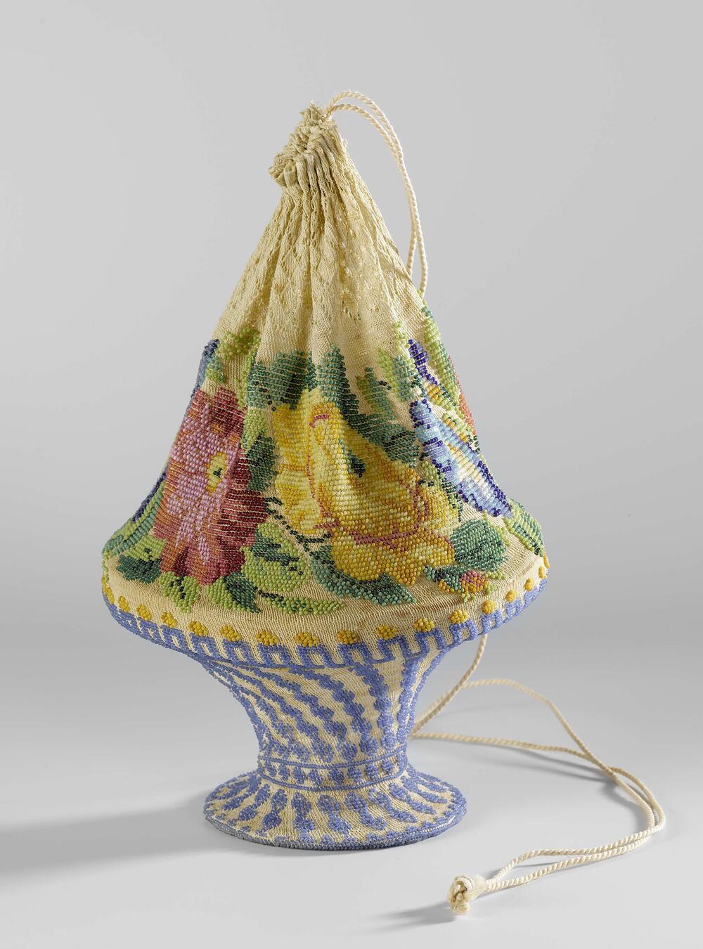 Reticule in de vorm van een bloemenmand, van ecrukleurig katoen, waarin veelkleurige kralen…