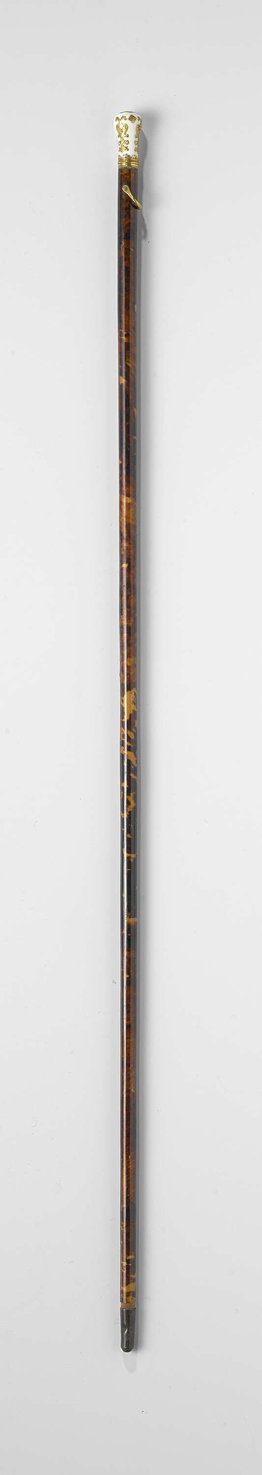 Dunne stok (badine) van hout belijmd met schildpad en voorzien van een knop van wit porseleinen,…