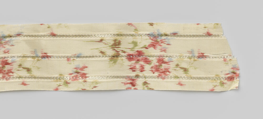 Rol chiné-lint (?) met drie banen ajourwerk en gedrukt bloemmotief in rose, groen en blauw