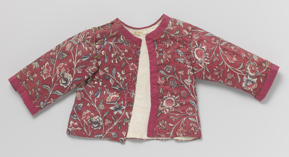 Jasje voor baby van sits met een rood fond, langs de mouwen, hals en langs één voorpand afgebiesd…