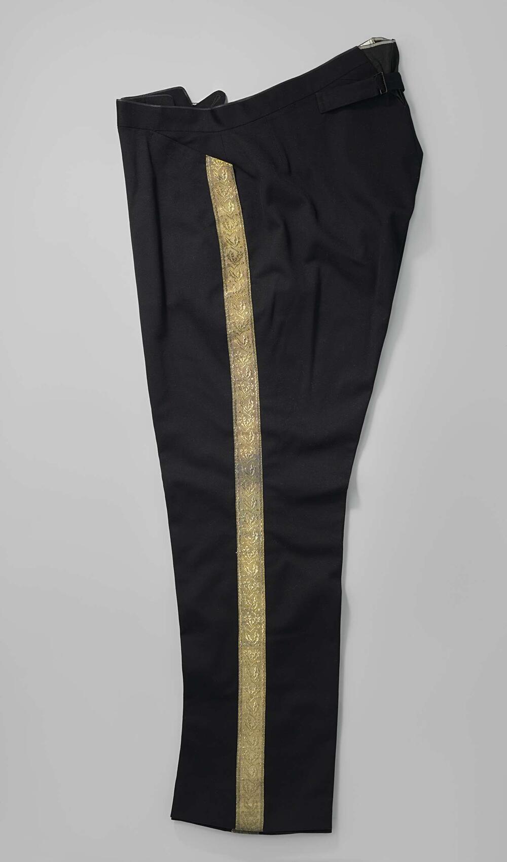Broek van zwart laken met lange pijpen en opgenaaide tailleband, vanachter met losse banden met een…