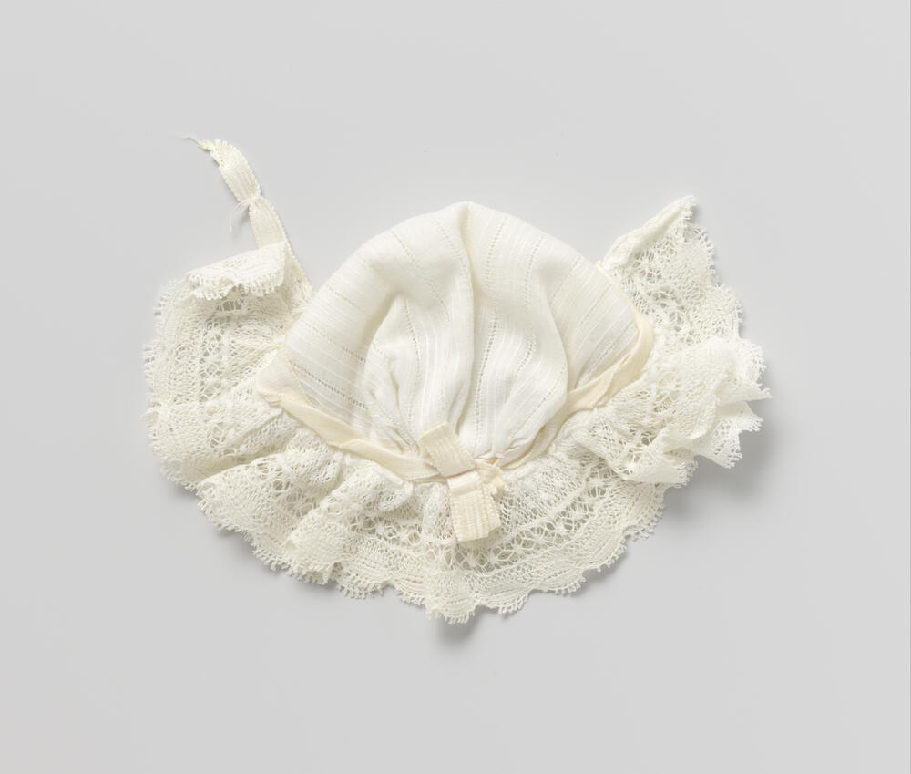 Poppenmuts van neteldoek, met kantstroken en roze lint