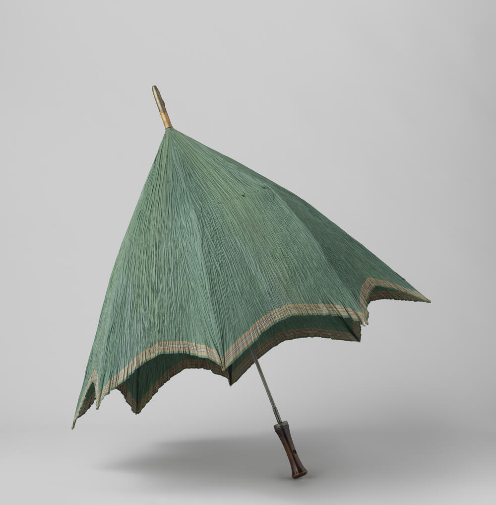 Parasol met dek van groene zijde met ingeweven streep langs de rand, op een ijzeren stok waaraan…
