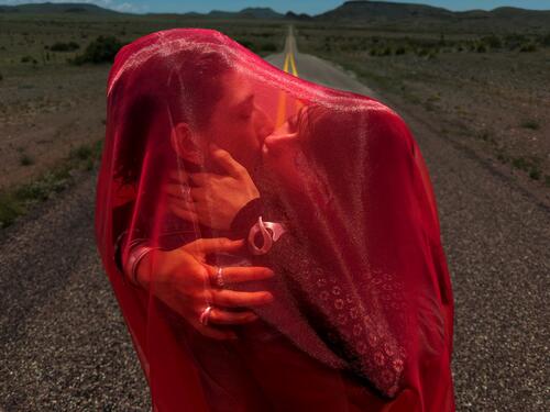 Twee zoenende mensen op een weg onder een rode voile