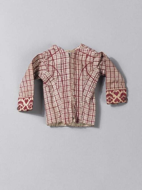 Een poppenjakje van Hindelooper bont, langs de onderkant van de mouwen rood langet, gevoerd met…