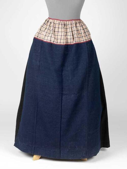Net blauw werkschort met strook van wit, blauw en rood bont en rood kloskanten tussenzetsel