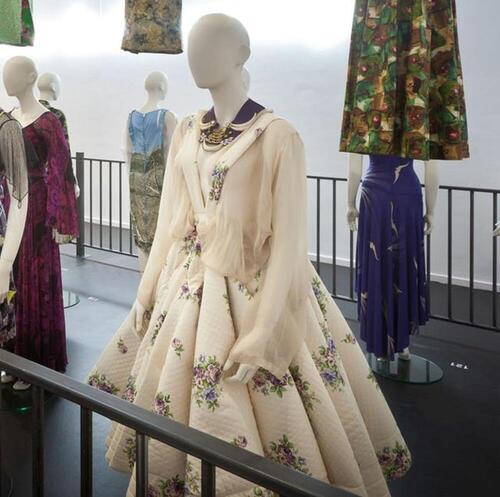 Ensemble bestaande uit witte blouse en rok met paarse bloemen met gebloemde broek en halsketting