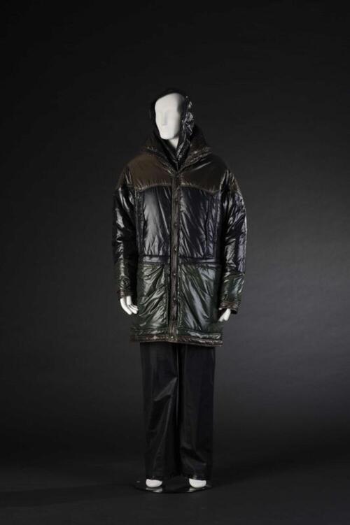 Ensemble bestaande uit gewatteerde parka in groen-bruin-zwarte, glanzende stof, zwarte, leren broek…