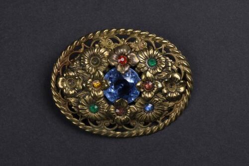 Broche in metaal met versiering van groene, blauwe, oranje en rode stenen