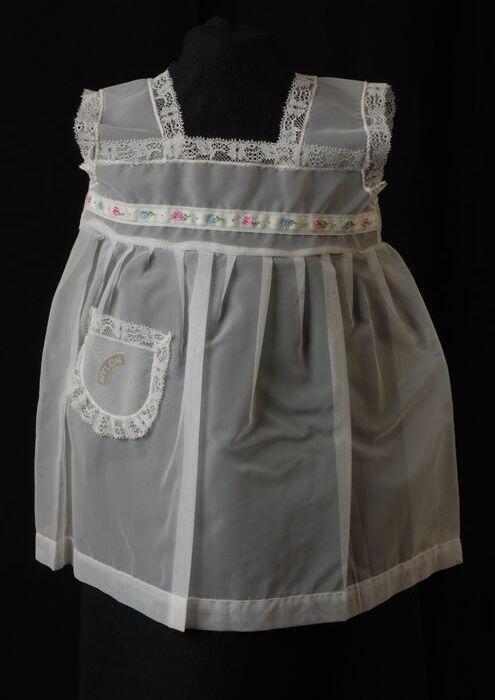 Babyjurk, mouwloos schortmodel van transparant wit nylonmet gebloemd randje, 'Femifra' model 'Aida'
