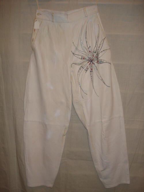 Broek van wit leer met op het linker bovenbeen een geborduurde bloem met zilver en rood,  onderdeel…