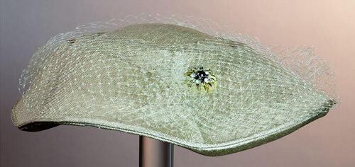 Dameshoed van beige stro met ingeperste belijning, overtrokken met beige voile, garnering met…