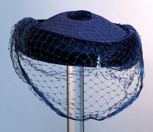 Ronde toque, donkerblauw vilt, rand en stofknoop van fluweel, garnering voile over de helft van de…